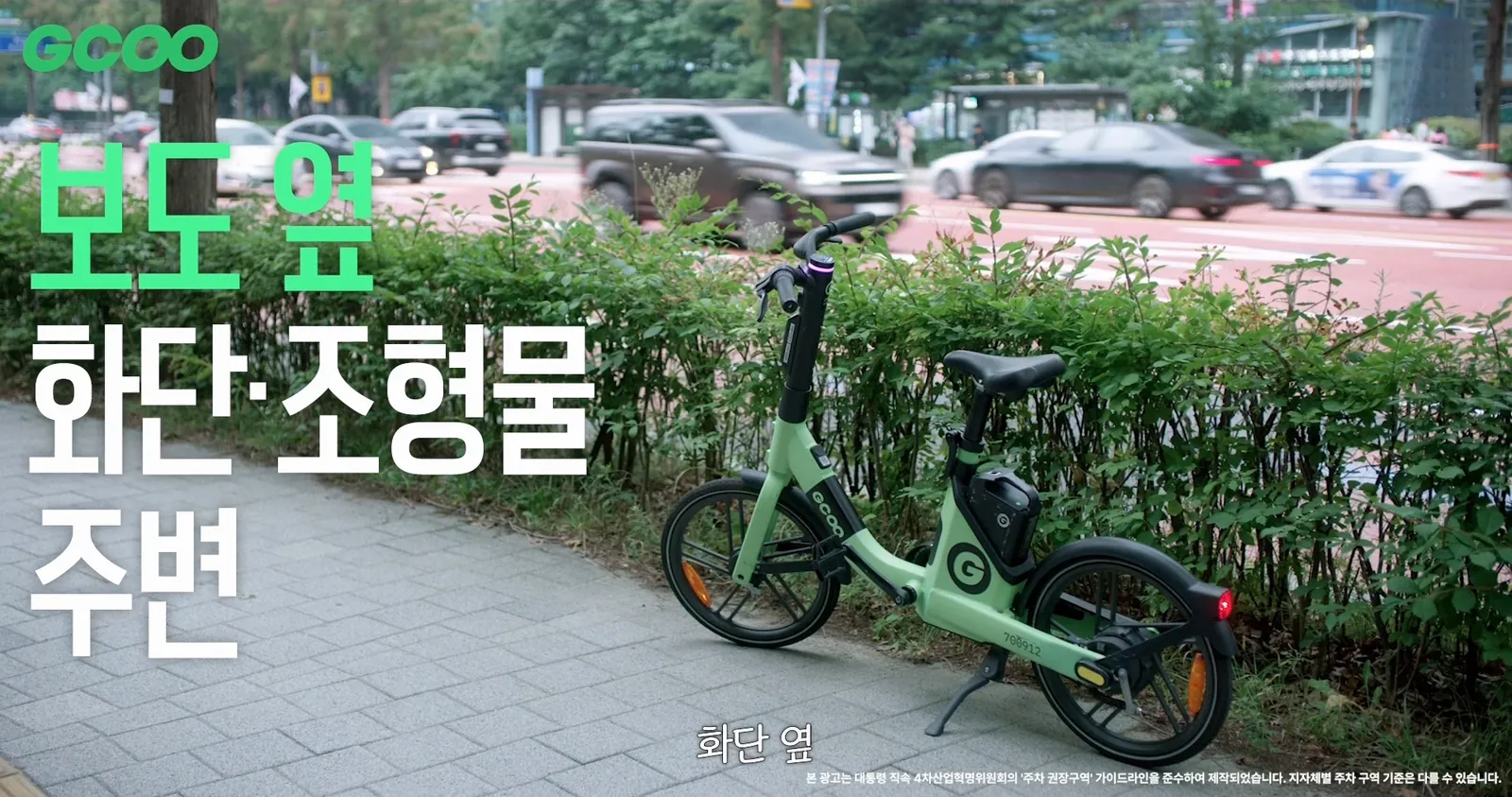 A GCOO bike parked in front of a flowerbed beside the sidewalk, with the on-screen text ‘Around flowerbeds and sculptures beside the sidewalk’