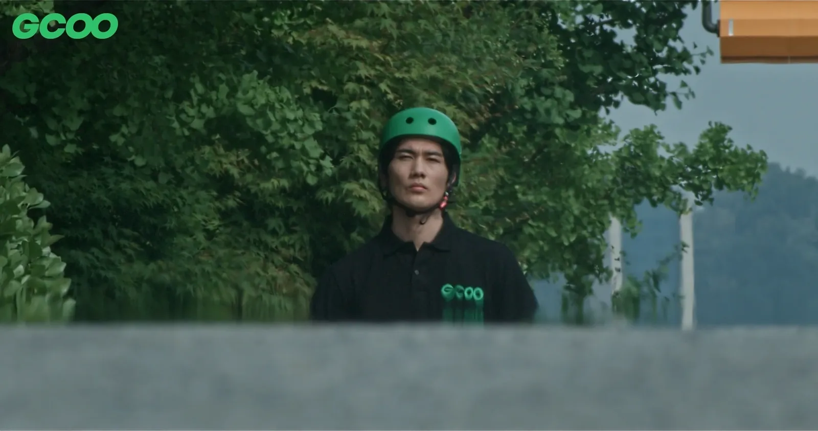 Um Tae-goo as the field operations staffer in a green helmet, standing in front of trees