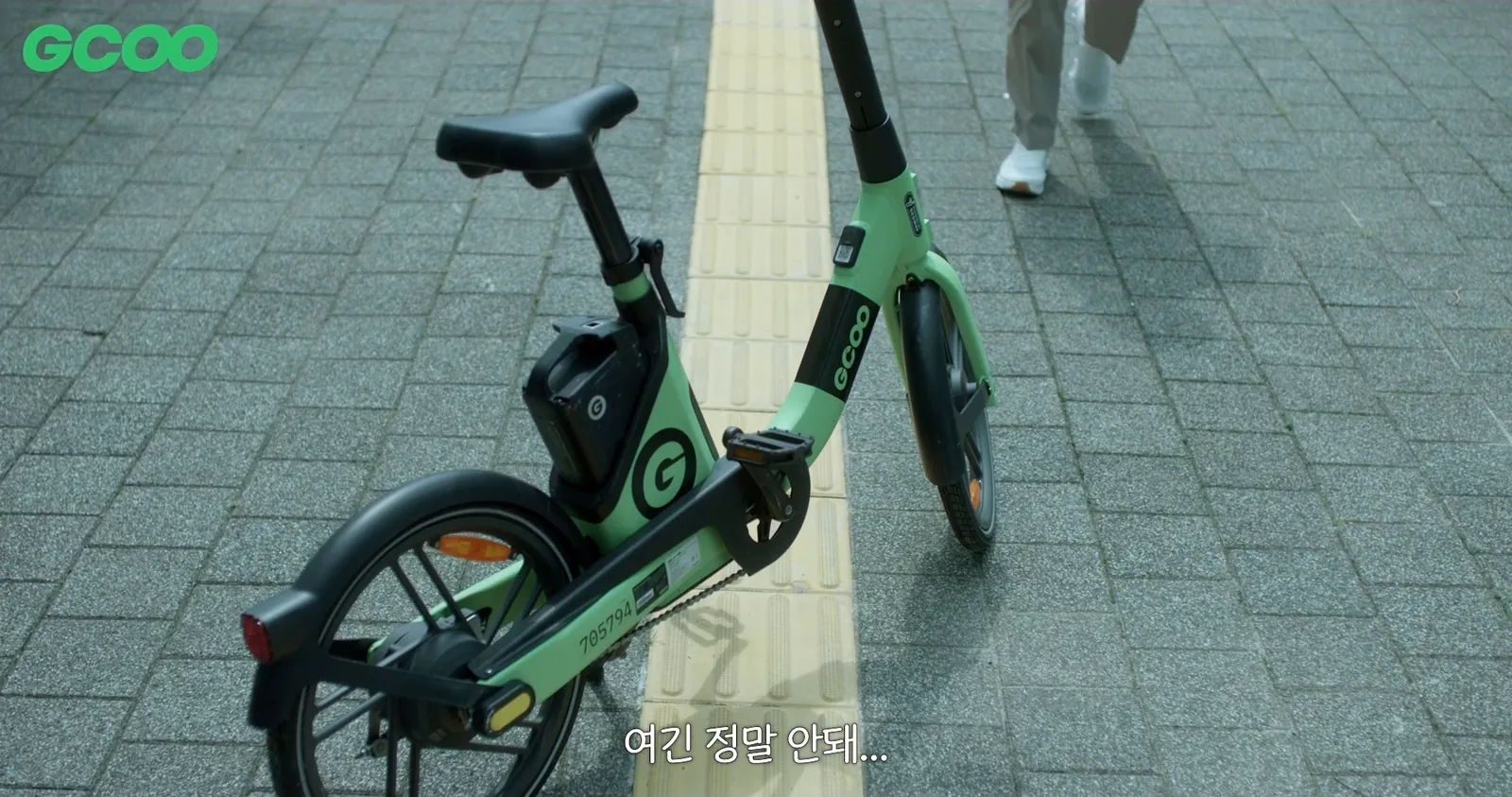 A GCOO bike parked on tactile paving, with a passerby’s feet